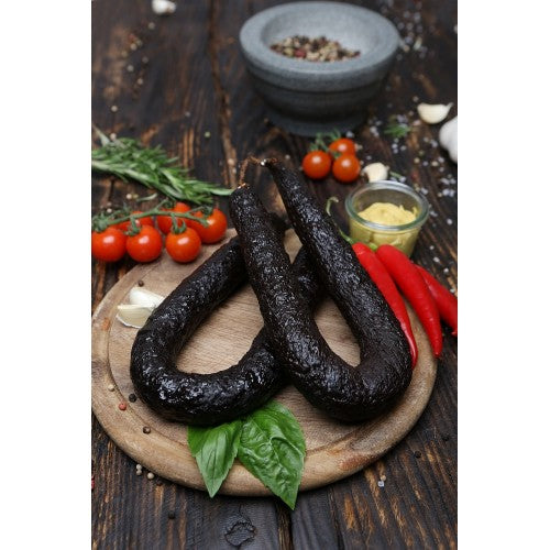 Schwarzwurst im Ring auf Holzbrett mit Gemüse garniert